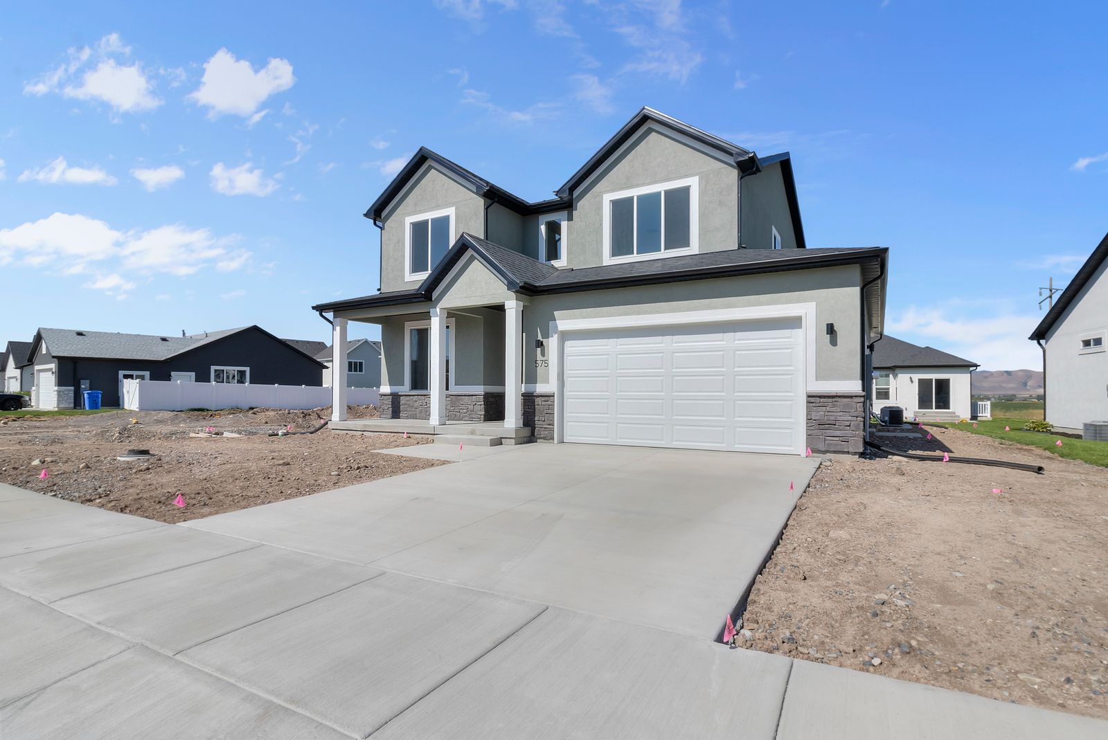 View of front facade with covered porch, concrete driveway, stucco siding, stone siding, and a garage