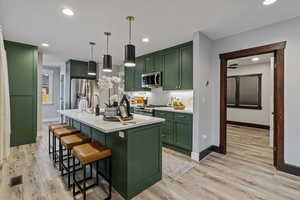 Kitchen featuring green cabinetry, light wood-type flooring, a kitchen island with sink, a breakfast bar area, and stainless steel appliances