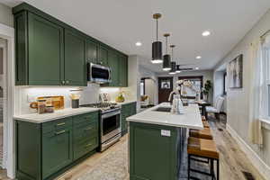 Kitchen with green cabinetry, stainless steel appliances, a center island with sink, light wood-style floors, and a breakfast bar