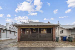 View of front of home with a shingled roof, brick siding, a chimney, and covered porch