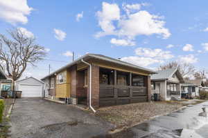 View of front of home with an outdoor structure, a garage, brick siding, and covered porch