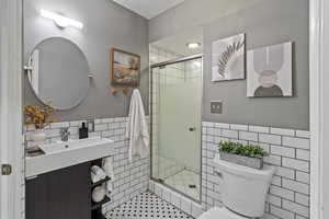 Full bath featuring tile walls, wainscoting, a shower stall, vanity, and pet washing station