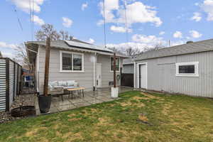 Rear view of house featuring roof mounted solar panels, an outdoor lounge area, a patio, an outbuilding, and a shingled roof