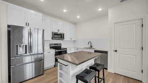 Kitchen with stainless steel appliances, a kitchen bar, white cabinets, light wood-style flooring, and backsplash