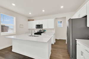 Kitchen with stainless steel appliances, a center island with sink, dark wood-type flooring, white cabinets, and recessed lighting