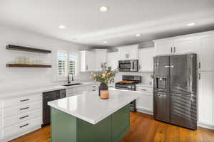 Dual tone kitchen featuring stainless steel appliances, dark wood-style flooring, open shelves, light stone countertops, and a center island