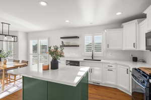 Kitchen with dark wood-style flooring, a center island, light stone counters, two tone cabinets, and open shelves
