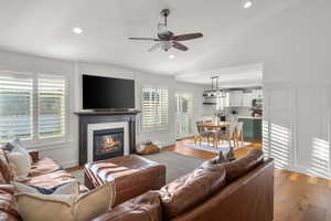 Living room with hardwood / wood-style flooring, a ceiling fan, a glass covered fireplace, vaulted ceiling, and a decorative wall