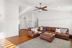 Living room featuring a decorative wall, wood-type flooring, lofted ceiling, a ceiling fan, and wainscoting