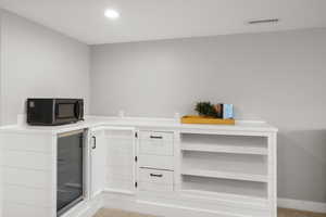 Bar area with white cabinets, light countertops, wine cooler, black microwave, and recessed lighting