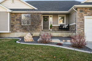 Property entrance featuring stone siding, a shingled roof, covered porch, and a lawn