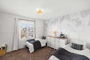 Bedroom featuring a decorative wall, a wainscoted wall, dark carpet, and wallpapered walls