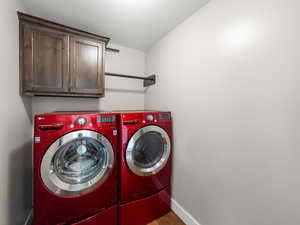Laundry area featuring a textured ceiling, washer and clothes dryer, cabinet space, and light wood-style floors