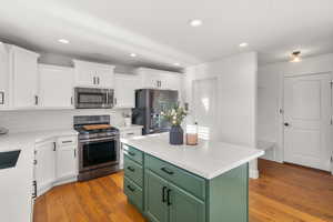 Kitchen featuring two tone cabinetry, stainless steel appliances, light stone countertops, light wood finished floors, and recessed lighting