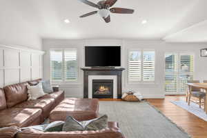 Living area featuring ceiling fan, wood finished floors, a glass covered fireplace, recessed lighting, and lofted ceiling