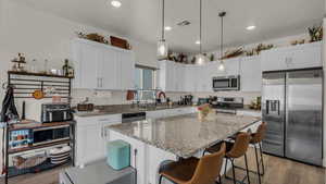 Kitchen featuring stainless steel appliances, light stone counters, white cabinets, and light wood finished floors