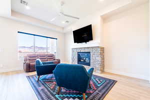 Living room with a tray ceiling, a ceiling fan, light wood-style floors, a stone fireplace, and recessed lighting