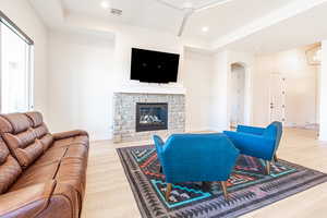 Living room with light wood-style floors, a stone fireplace, arched walkways, recessed lighting, and a ceiling fan