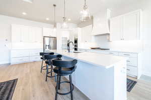 Kitchen featuring decorative backsplash, a breakfast bar, white cabinetry, hanging light fixtures, and a kitchen island with sink