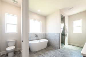 Bathroom with a stall shower, a soaking tub, tile walls, plenty of natural light, and recessed lighting