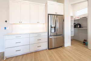 Kitchen featuring stainless steel fridge with ice dispenser, white cabinets, light wood-type flooring, and tasteful backsplash