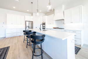 Kitchen with white cabinets, a kitchen breakfast bar, light wood finished floors, decorative light fixtures, and decorative backsplash