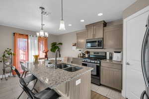 Kitchen with light stone countertops, stainless steel appliances, a kitchen breakfast bar, and a kitchen island with sink