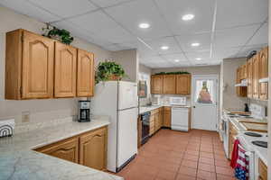Kitchen featuring white appliances, a paneled ceiling, light countertops, recessed lighting, and light tile patterned floors