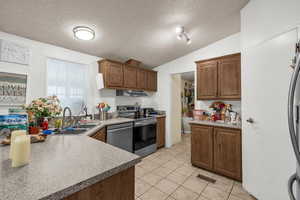 Kitchen featuring stainless steel appliances, wood finish cabinetry, light tile patterned floors, light countertops, and a peninsula