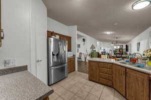 Kitchen with stainless steel refrigerator with ice dispenser, open floor plan, a textured ceiling, light tile patterned flooring, and a ceiling fan