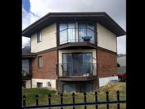 Back of house with brick siding, a balcony, and stucco siding
