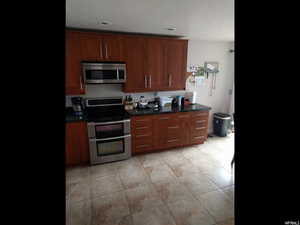 Kitchen featuring stainless steel appliances, wood finish cabinets, and dark stone countertops