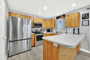 Kitchen featuring a peninsula, stainless steel appliances, light countertops, light wood-type flooring, and recessed lighting