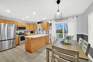 Kitchen featuring light countertops, stainless steel appliances, a peninsula, hanging light fixtures, and light wood-style floors