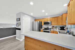Kitchen with stainless steel appliances, light countertops, a peninsula, light wood-type flooring, and recessed lighting