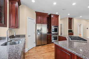 Kitchen featuring glass fronted cabinets, stainless steel appliances, dark stone counters, recessed lighting, and light wood-type flooring