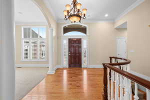 Entryway featuring crown molding, arched walkways, light wood finished floors, plenty of natural light, and hanging lights