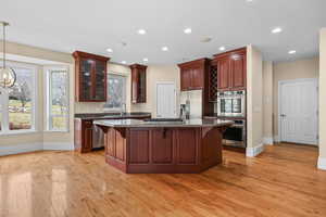 Kitchen with dark stone counters, glass insert cabinets, stainless steel appliances, a kitchen island, and light wood-style floors