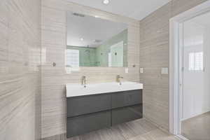 Bathroom featuring double vanity, tile walls, a shower stall, and recessed lighting
