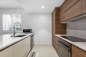 Kitchen with stainless steel appliances, modern cabinets, light stone counters, recessed lighting, and wood finish cabinets