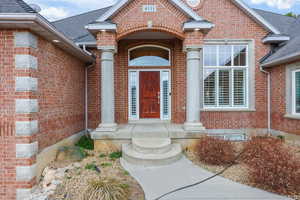 View of exterior entry with brick siding and roof with shingles