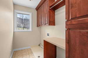 Laundry area with hookup for a washing machine, a desk, light tile patterned flooring, and cabinet space