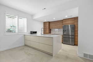 Kitchen with modern cabinets, stainless steel appliances, a peninsula, wood finish cabinetry, and light stone counters