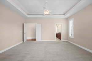 Unfurnished bedroom featuring light carpet, ensuite bath, ceiling fan, and a raised ceiling