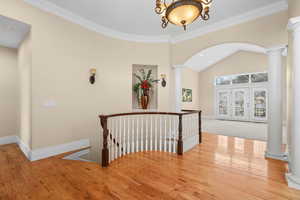 Hallway with vaulted ceiling, hardwood / wood-style floors, decorative columns, ornamental molding, and an upstairs landing