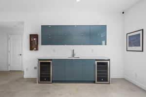 Indoor wet bar with modern cabinets, blue cabinetry, wine cooler, and light stone countertops