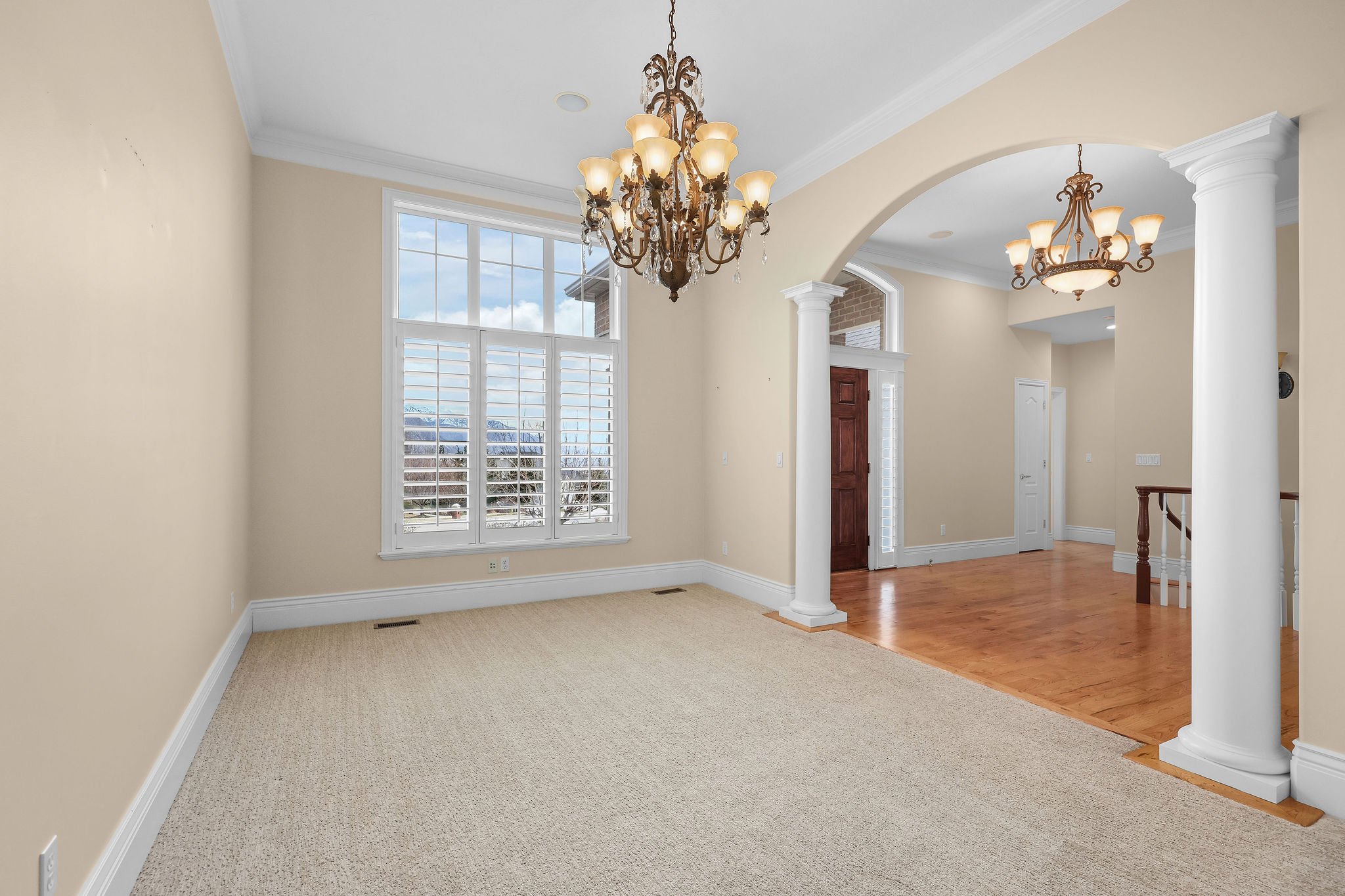 Spare room featuring ornate columns, light carpet, arched walkways, a chandelier, and crown molding