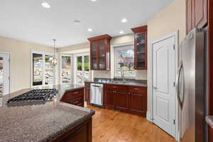 Kitchen with stainless steel appliances, glass fronted cabinets, dark stone countertops, light wood finished floors, and hanging light fixtures