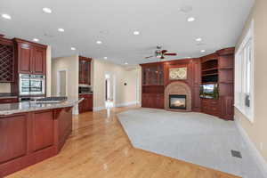 Kitchen featuring arched walkways, a brick fireplace, recessed lighting, light wood-type flooring, and light stone counters