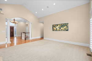 Empty room with vaulted ceiling, recessed lighting, arched walkways, light carpet, and decorative columns
